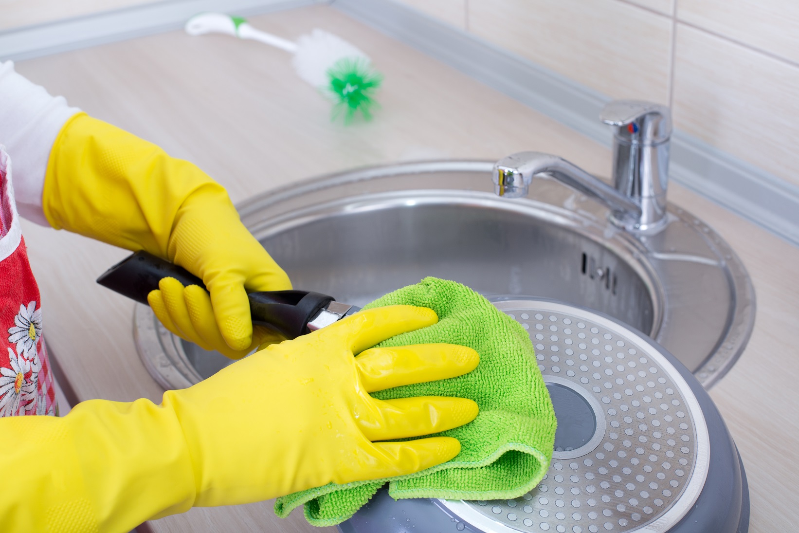 Close up of female hands with rubber gloves cleaning frying pan in the kitchen