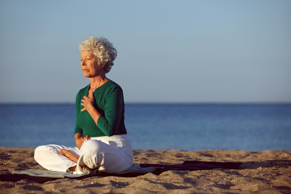 Eldery woman doing yoga on beach