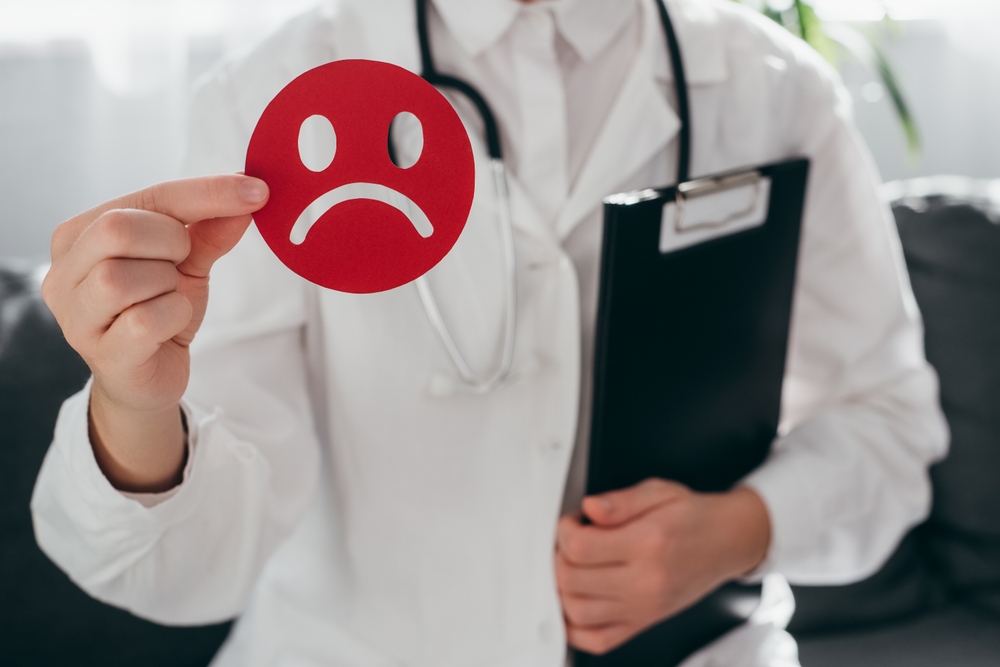 Woman doctor in white uniform with stethoscope holding little red angry emoticon