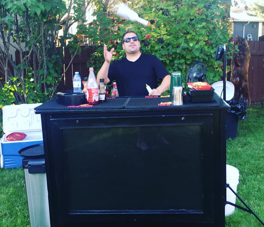 Person flipping bottle at a backyard house party behind portable bar