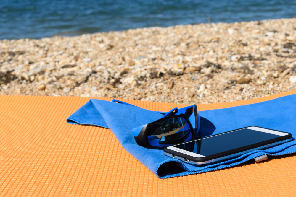 Sun goggles lying on a microfiber towel next to the mobile on the travel Mat
