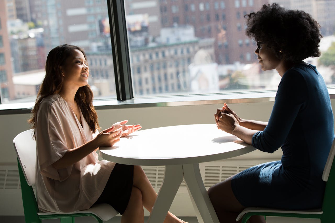 Photography of Women Talking to Each Other while sitting on a table