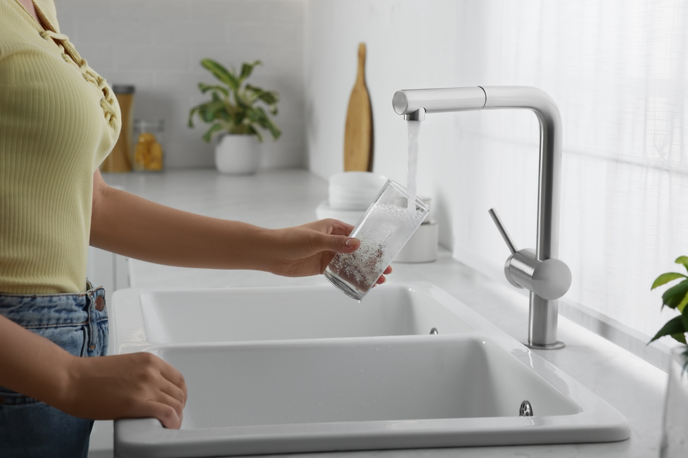 Woman filling glass with water from tap in kitchen