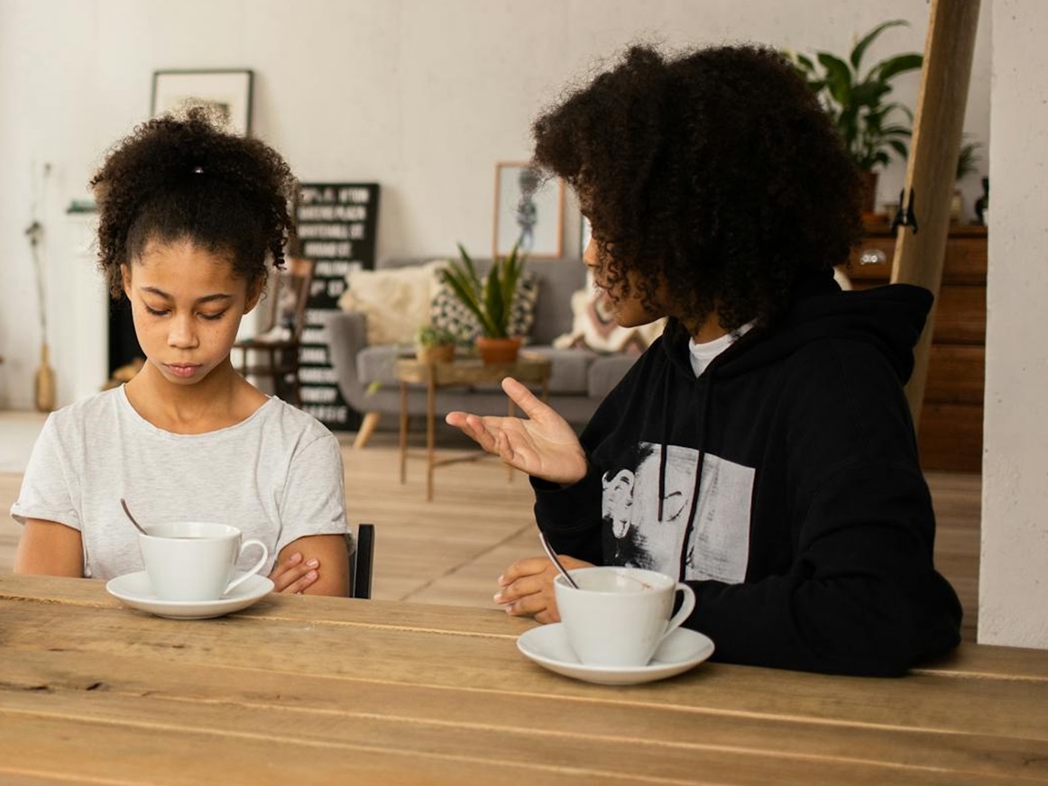Mother lecturing upset daughter at table.