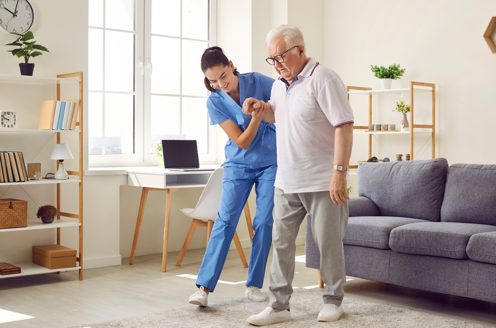 Young nurse helping elderly man walk in the room
