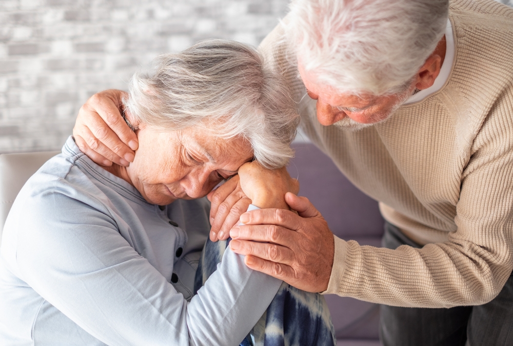 Senior man comforting his depressed illness wife, unhappy elderly woman at home