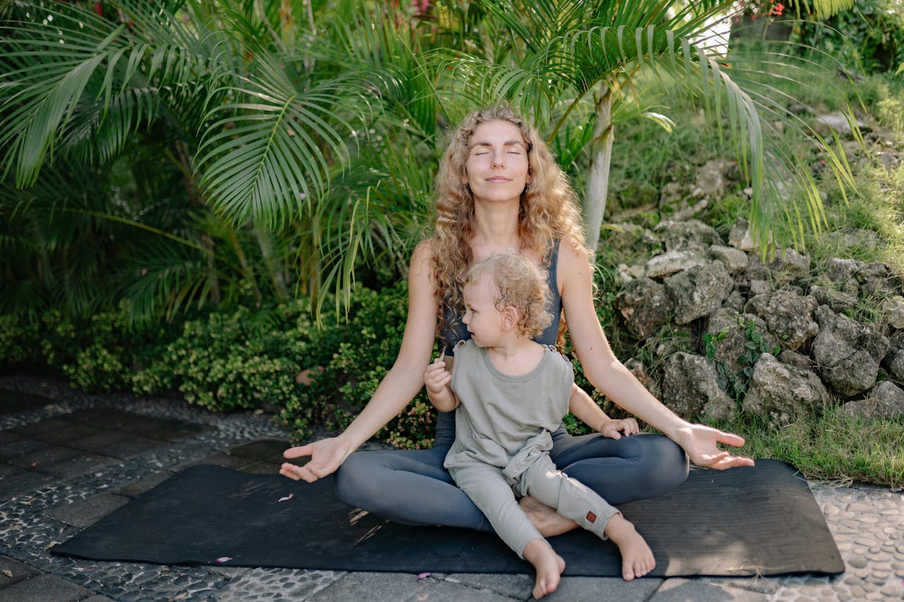 Cheerful sportswoman meditating in lotus pose with son