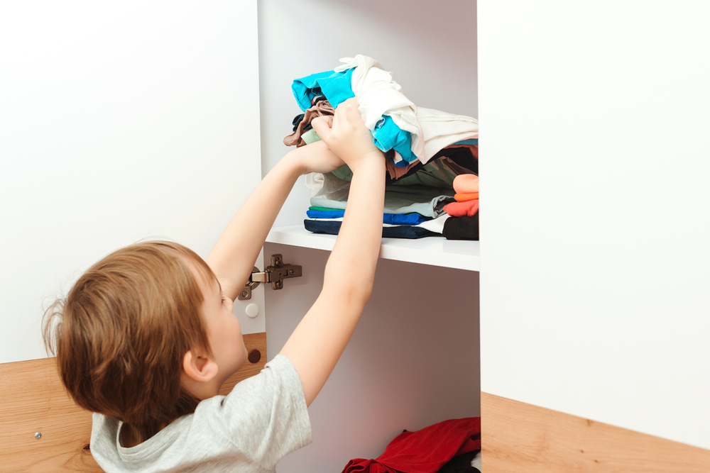 The boy puts things in order in the closet