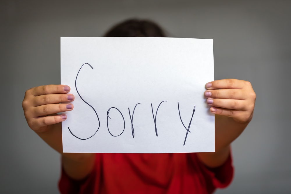 A girl holding up a paper saying sorry