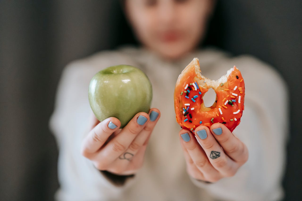 Photo of Woman showing apple and bitten doughnut