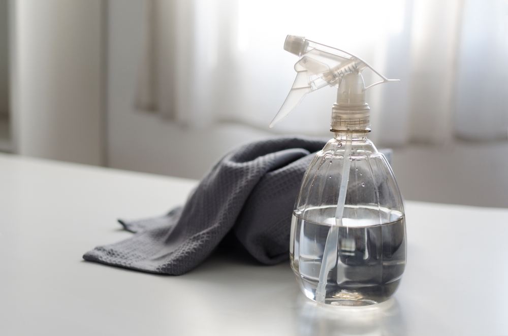 Spray bottle filled with pure water and vinegar and a cleaning cloth on a table