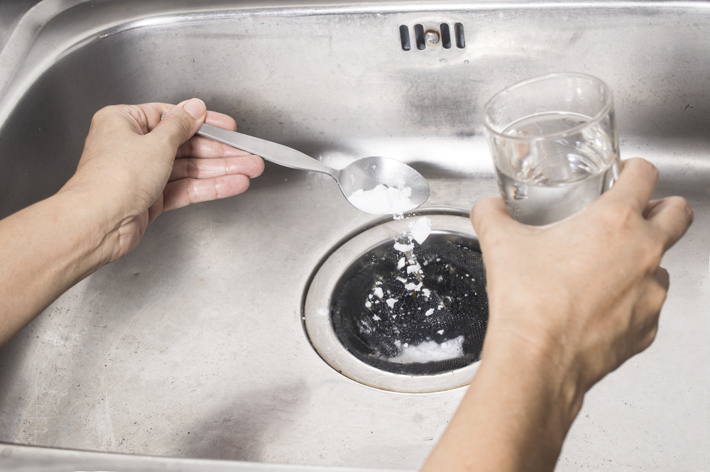 Person pouring a spoon of baking soda and a glass of vinegar into the drain of sink