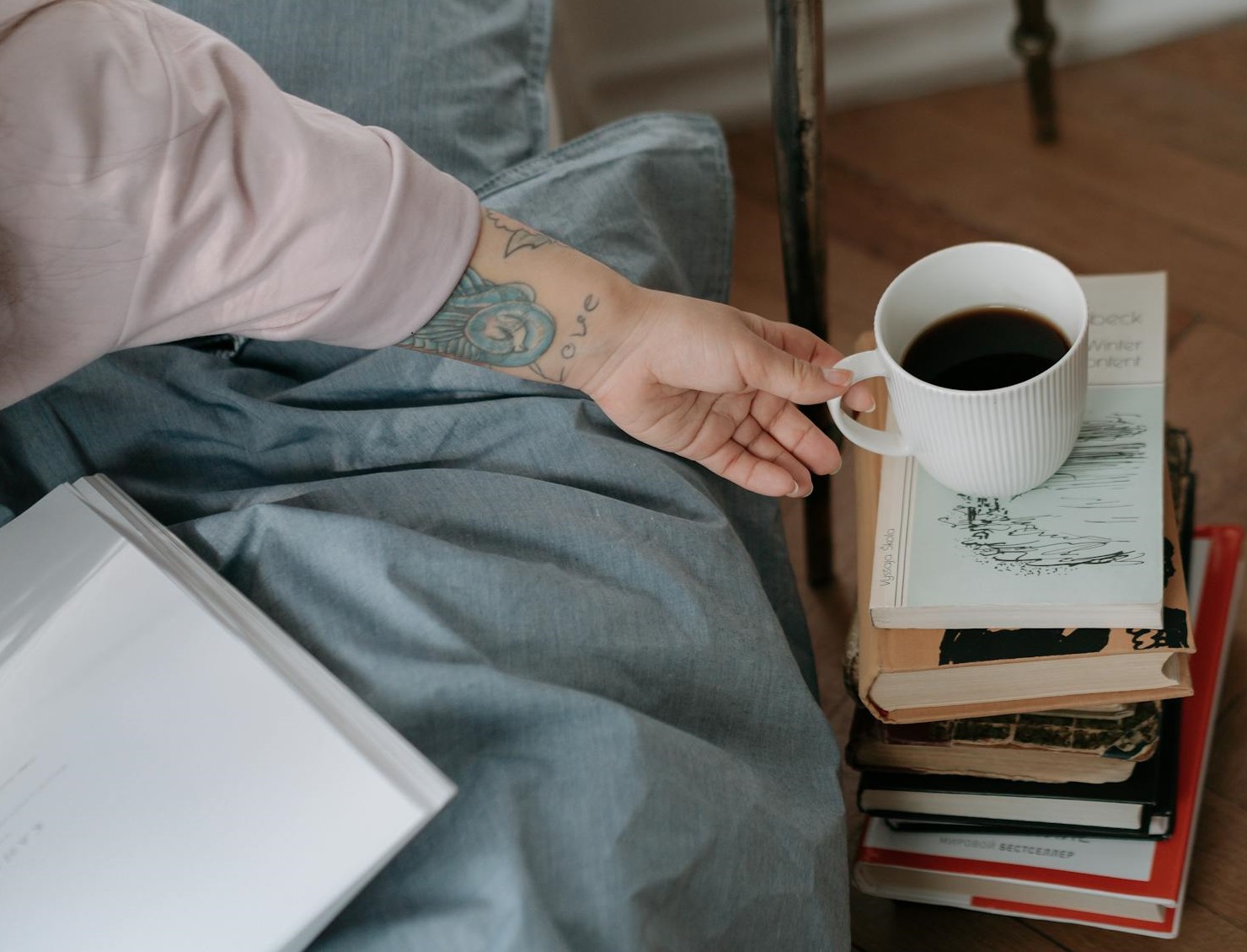 Hand taking a cup of coffee from the pile of books