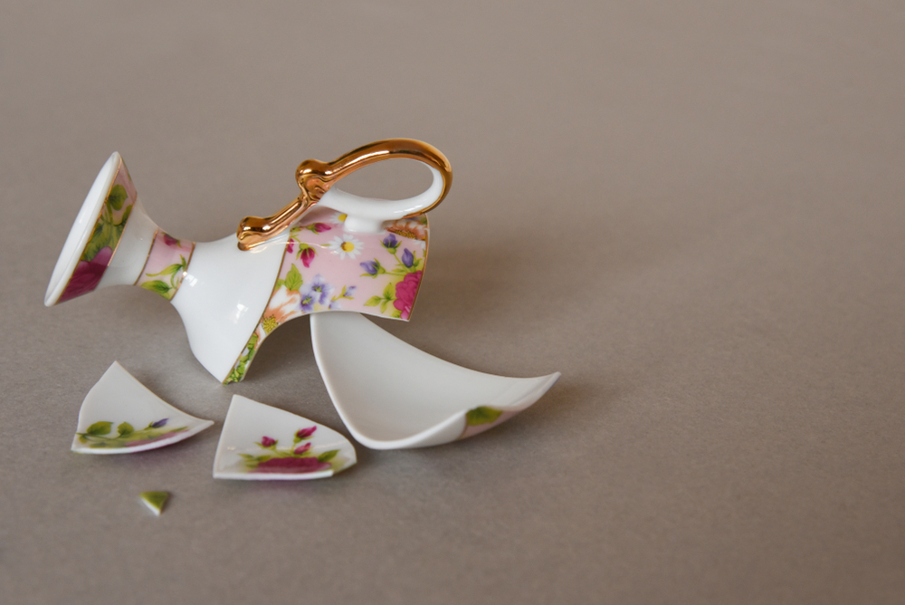 Broken in pieces pink porcelain tea cup with floral design on plate.