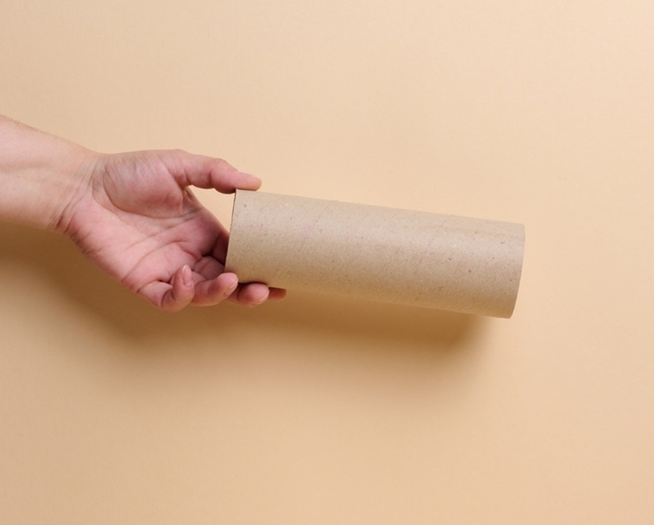 A woman's hand holds a brown paper tube from paper towels