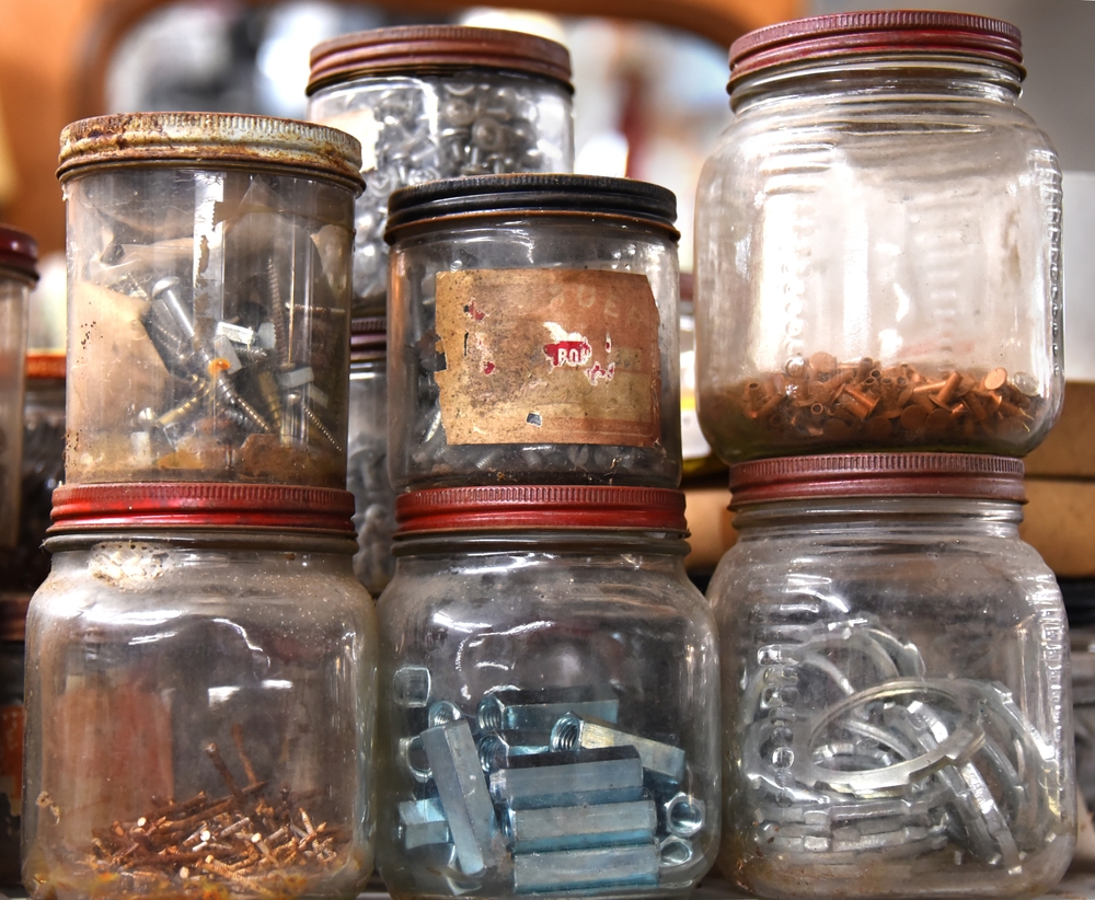 Old jars with red metal lids store miscellaneous hardware. Contents include screws, bolts, nails and nuts.