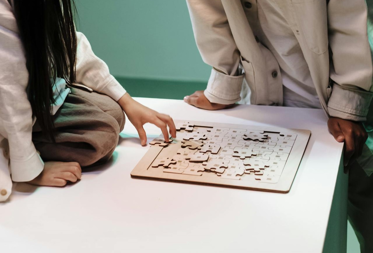 Two kids leaning over puzzle laying on table