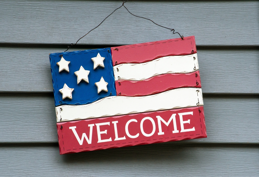 A decorative American flag made of wood, hangs on the side of a home by the front door