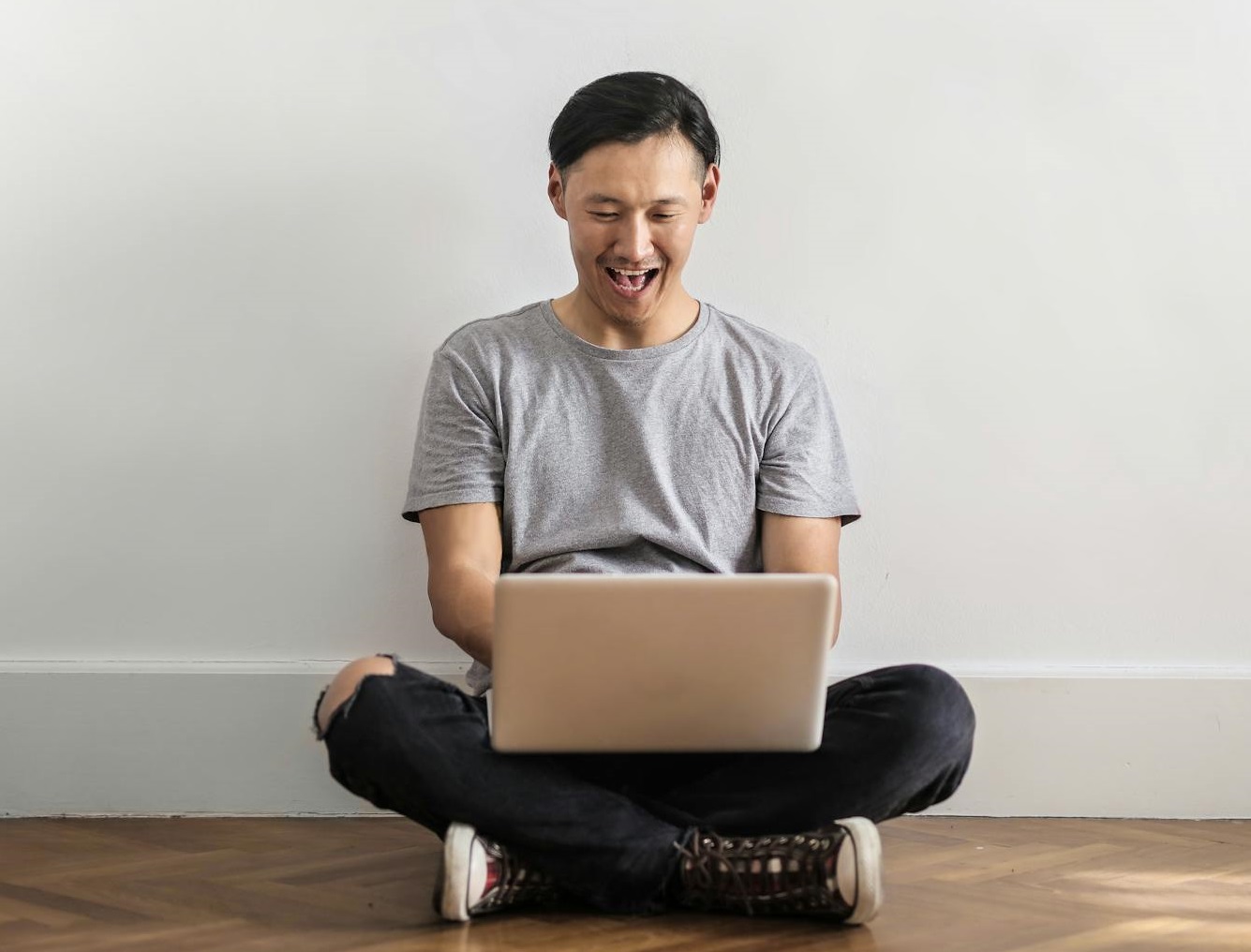 Smiling man Sitting on Wooden Floor While Using a Laptop