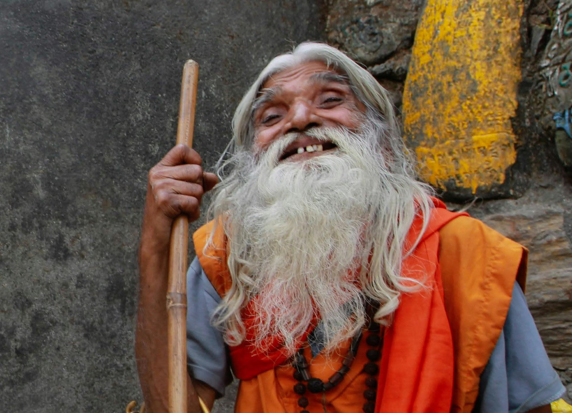 An Elderly Man in Traditional Clothes Smiling and holding a stick.