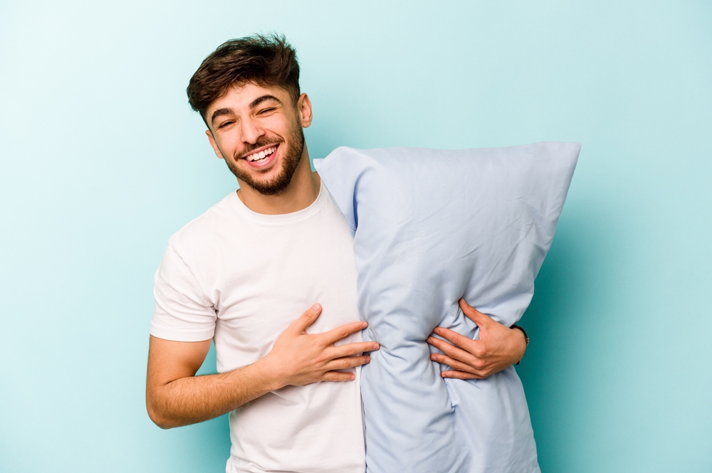 Young man wearing a pajama holding pillow and smiling.