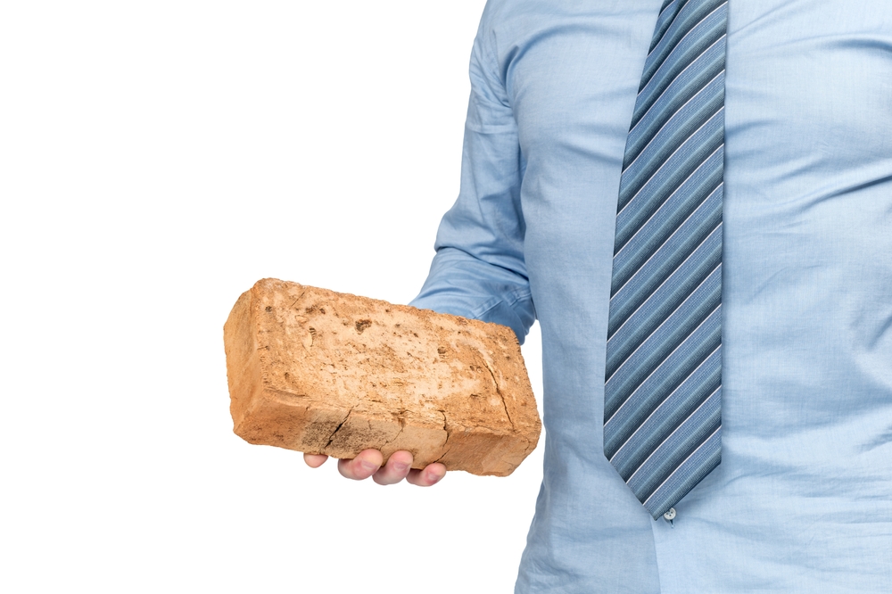 A man in a blue shirt and tie holds an orange brick in his hand