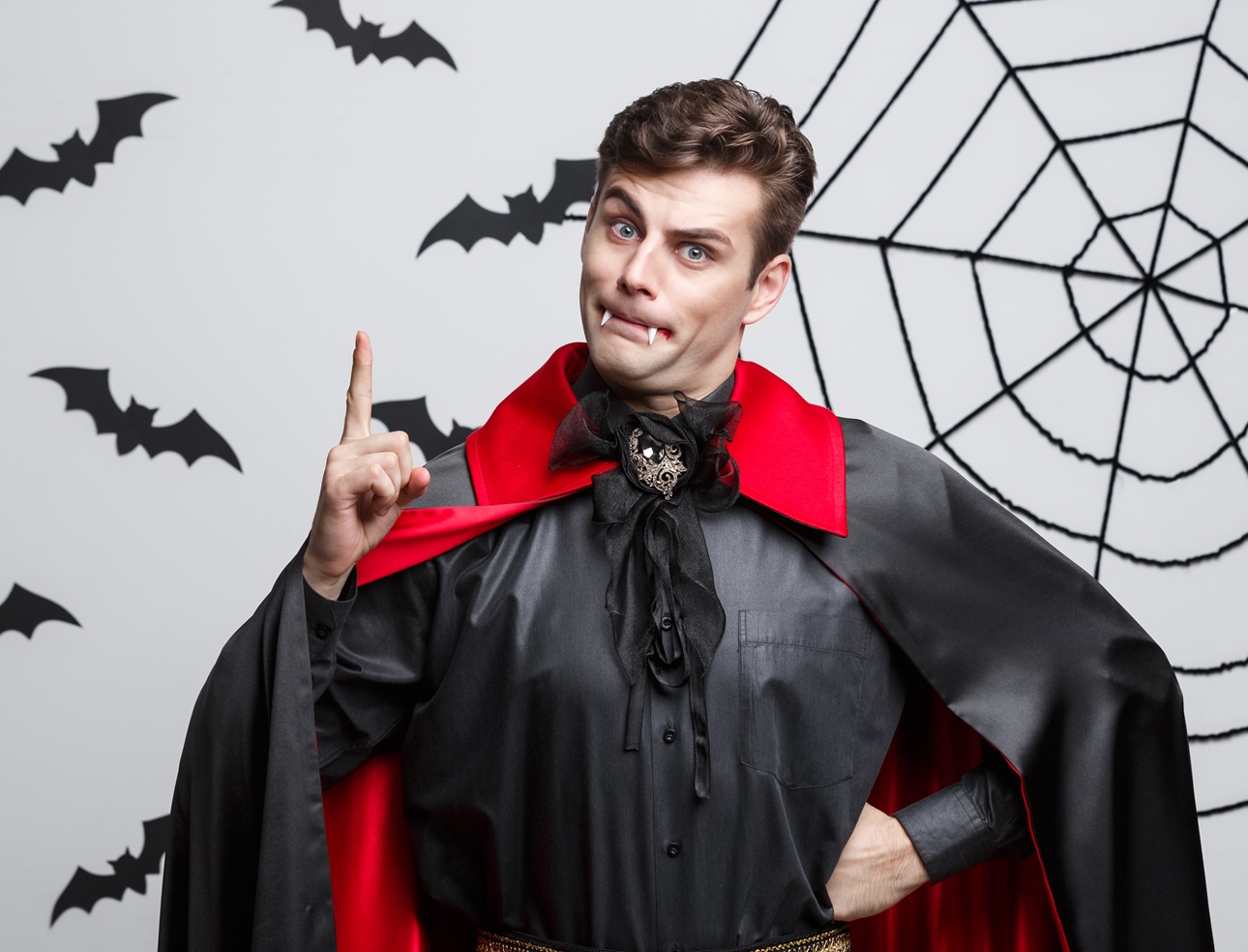 Portrait of handsome caucasian in Vampire halloween costume pointing on side.
