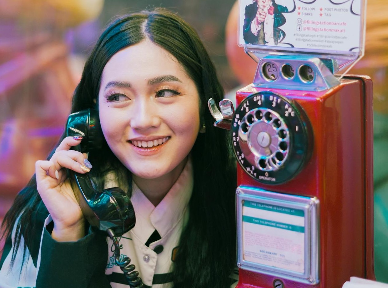Smiling Young Woman Using a Retro Pay Phone