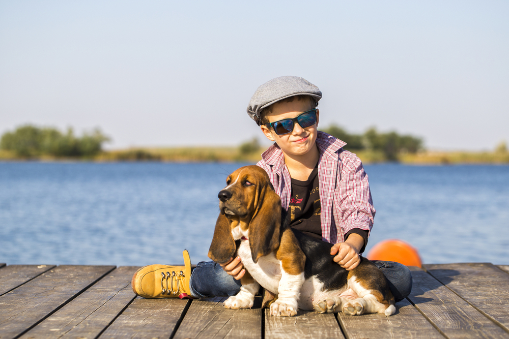 Little cute boy is sitting by the river with his dog.