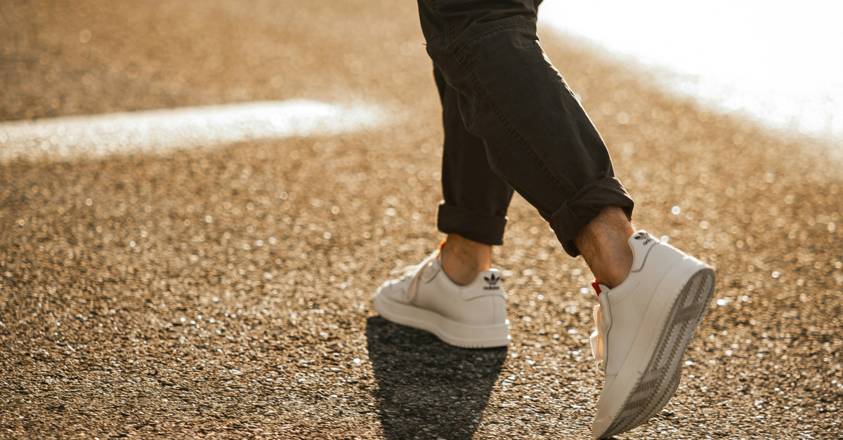 person in black pants and white sneakers walking on brown asphalt road during daytime