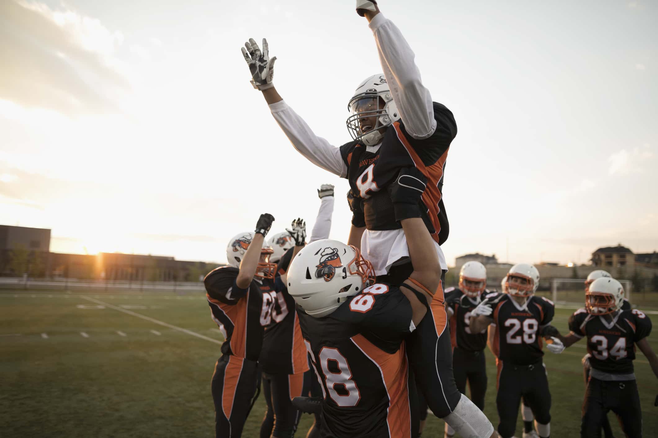 Teenage boy high school football players lifting celebrating, cheering teammate on football field