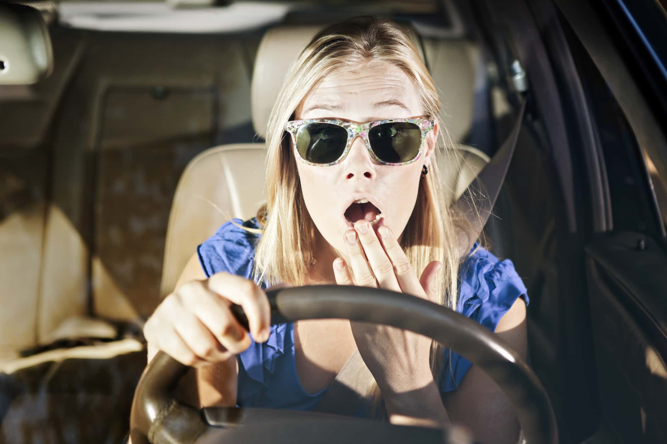 Horrified blonde drive with hand to mouth, looks through windscreen.